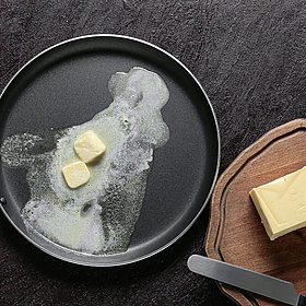 Schmelzende Butter in einer Pfanne, daneben ein Holzbrett mit Butterstückchen
