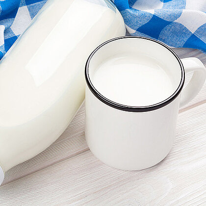 Ein Becher Milch neben einer Milchflasche
