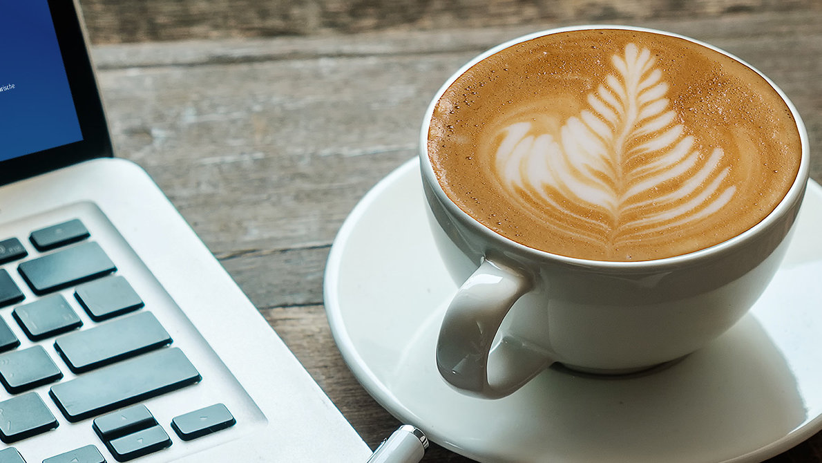 Ein Laptop, daneben ein Cappuccino mit Latte Art
