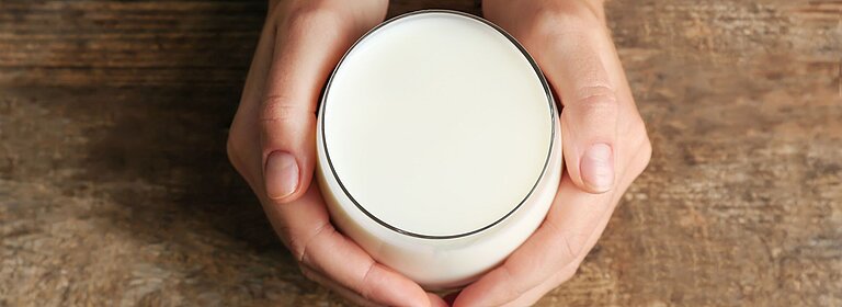Hände umschließen ein Glas Milch